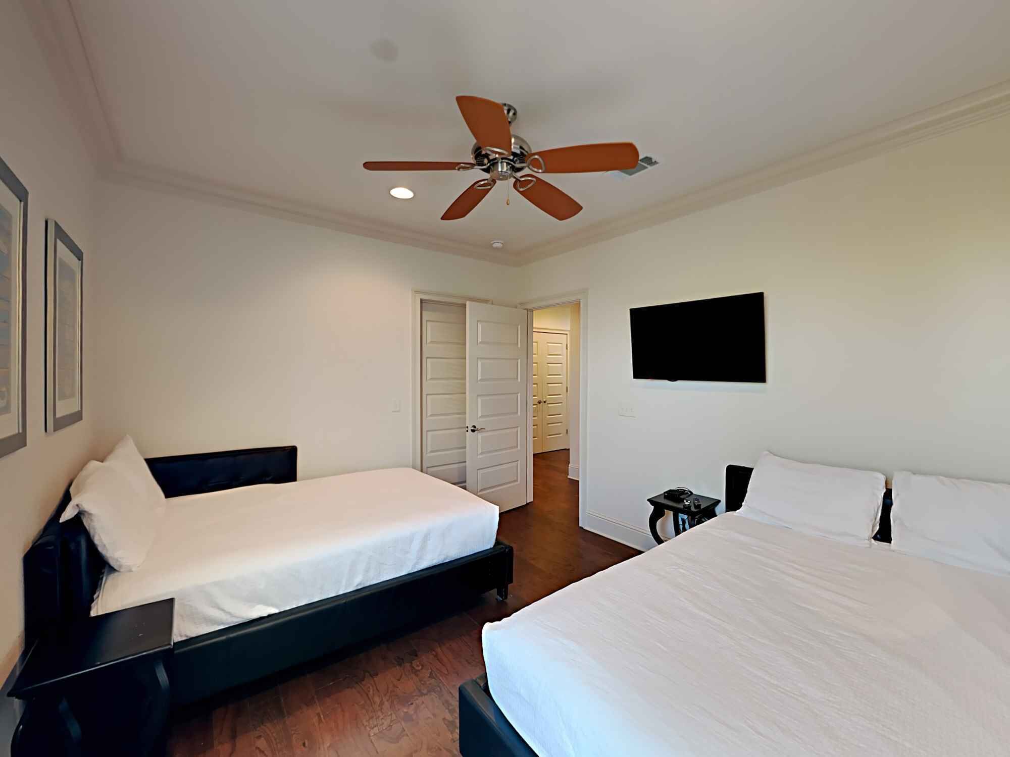 Une chambre d’hôtel avec deux lits, un ventilateur de plafond, un téléviseur fixé au mur et une porte donnant sur une autre chambre.