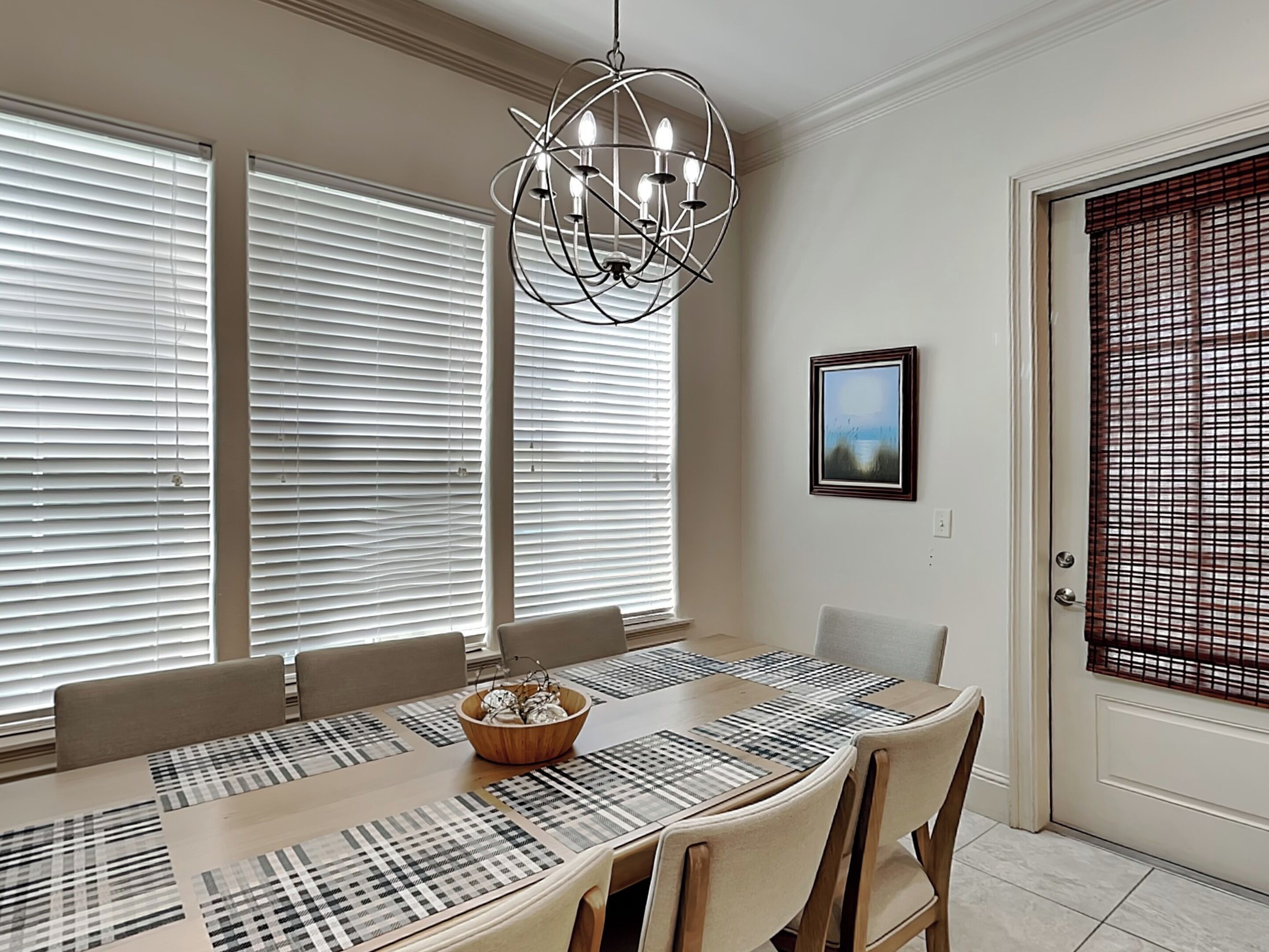 A dining room with a large table, chairs, a chandelier, and a door with a screen.