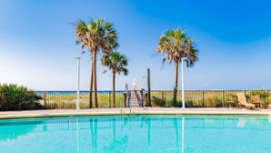 Une piscine d’un bleu éclatant, bordée d’une rambarde en métal, entourée de palmiers et offrant une vue sur la plage.