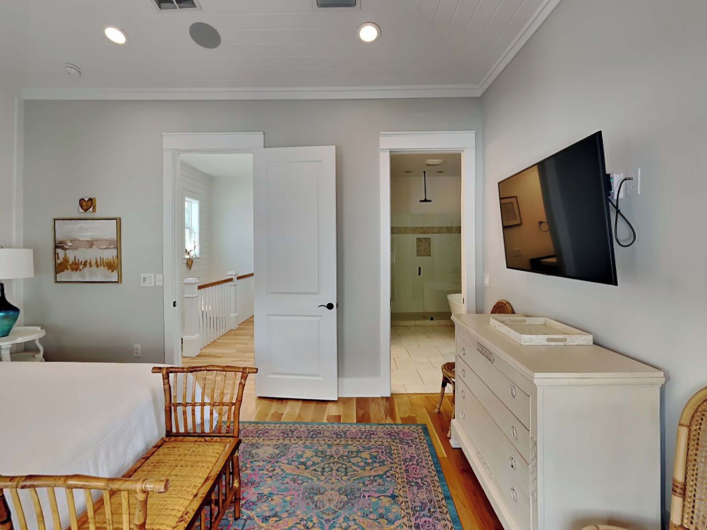 A hotel room with a bed, a desk, a chair, a dresser, a television, and a shower area.