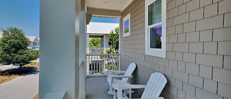 A porch with white rocking chairs, a white railing, and a view of a street and trees.