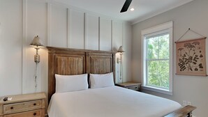 Ein Schlafzimmer mit Holzkopfteil, einem großen Bett, Nachttischen und einem Fenster mit Blick auf Bäume.