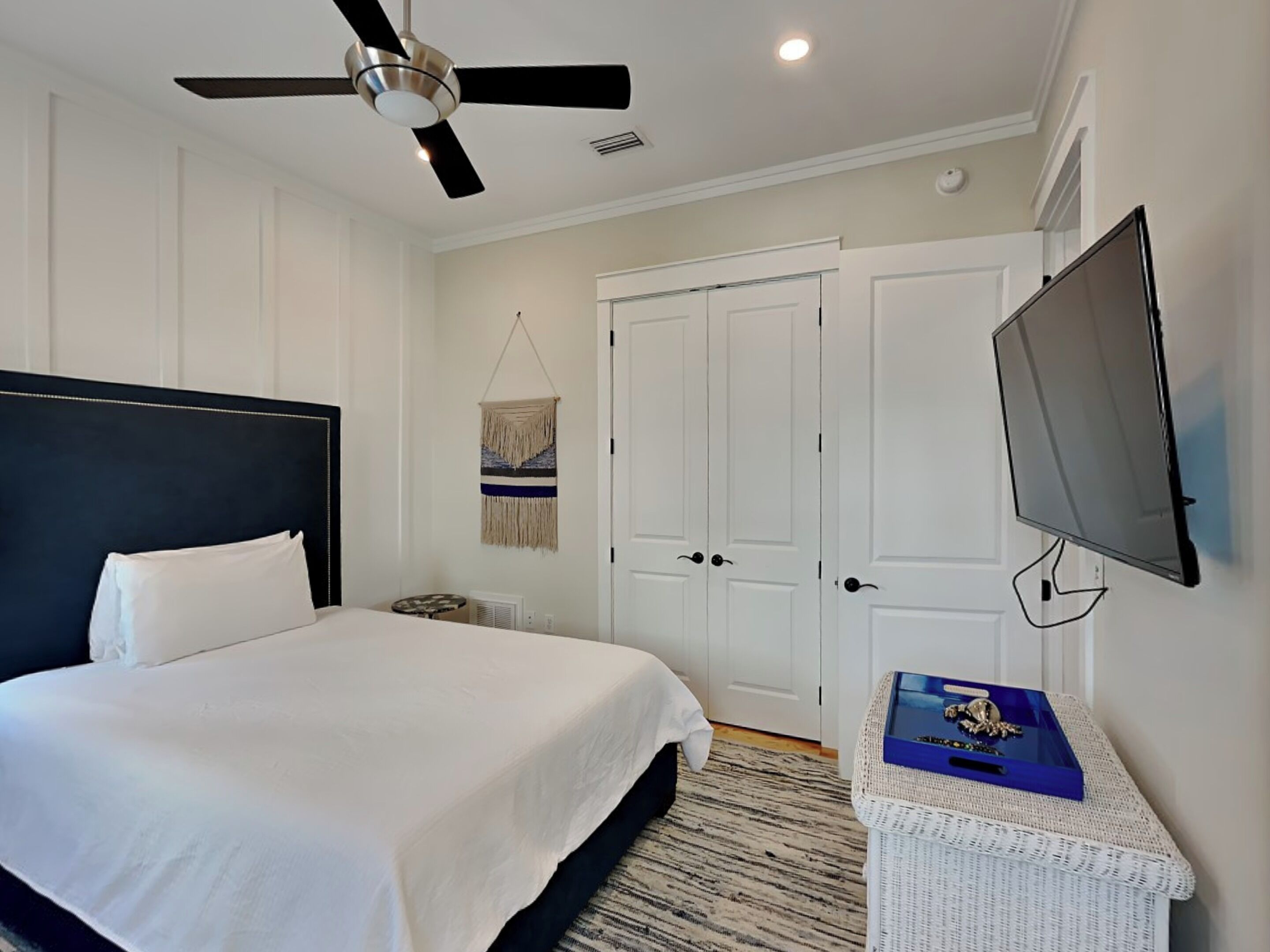 A bedroom with a bed, a ceiling fan, a TV, and a door.