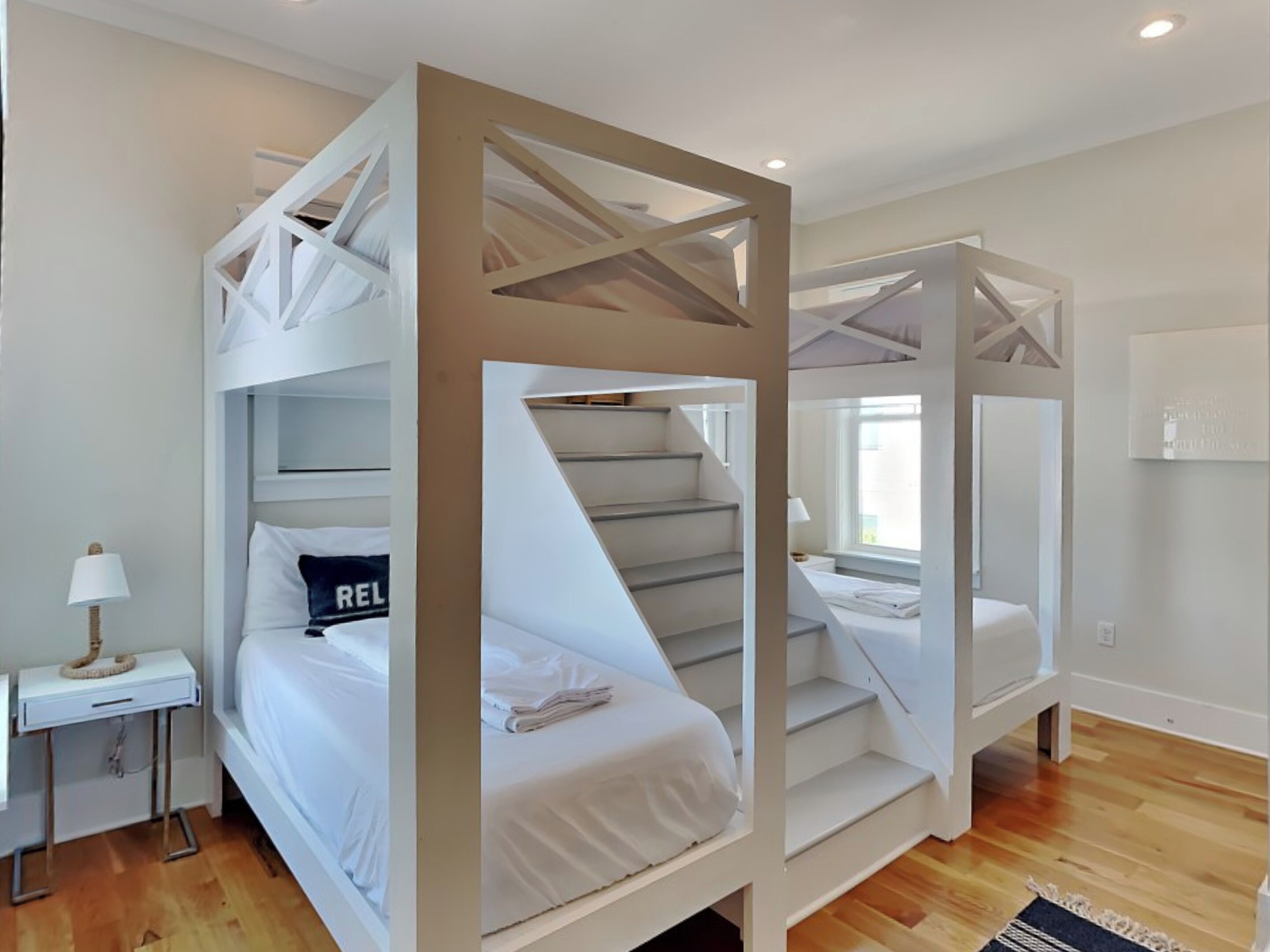 Ett modernt hotellrum med våningssängar, ett nattduksbord med en lampa och utsikt över staden.
