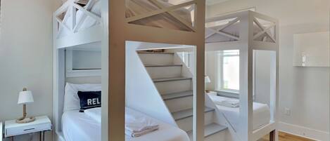 A modern hotel room with bunk beds, a bedside table with a lamp, and a view of the city.