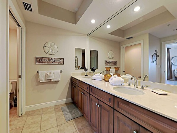 Un baño con un espejo grande, dos lavamanos, armarios de madera y relojes decorativos en la pared.