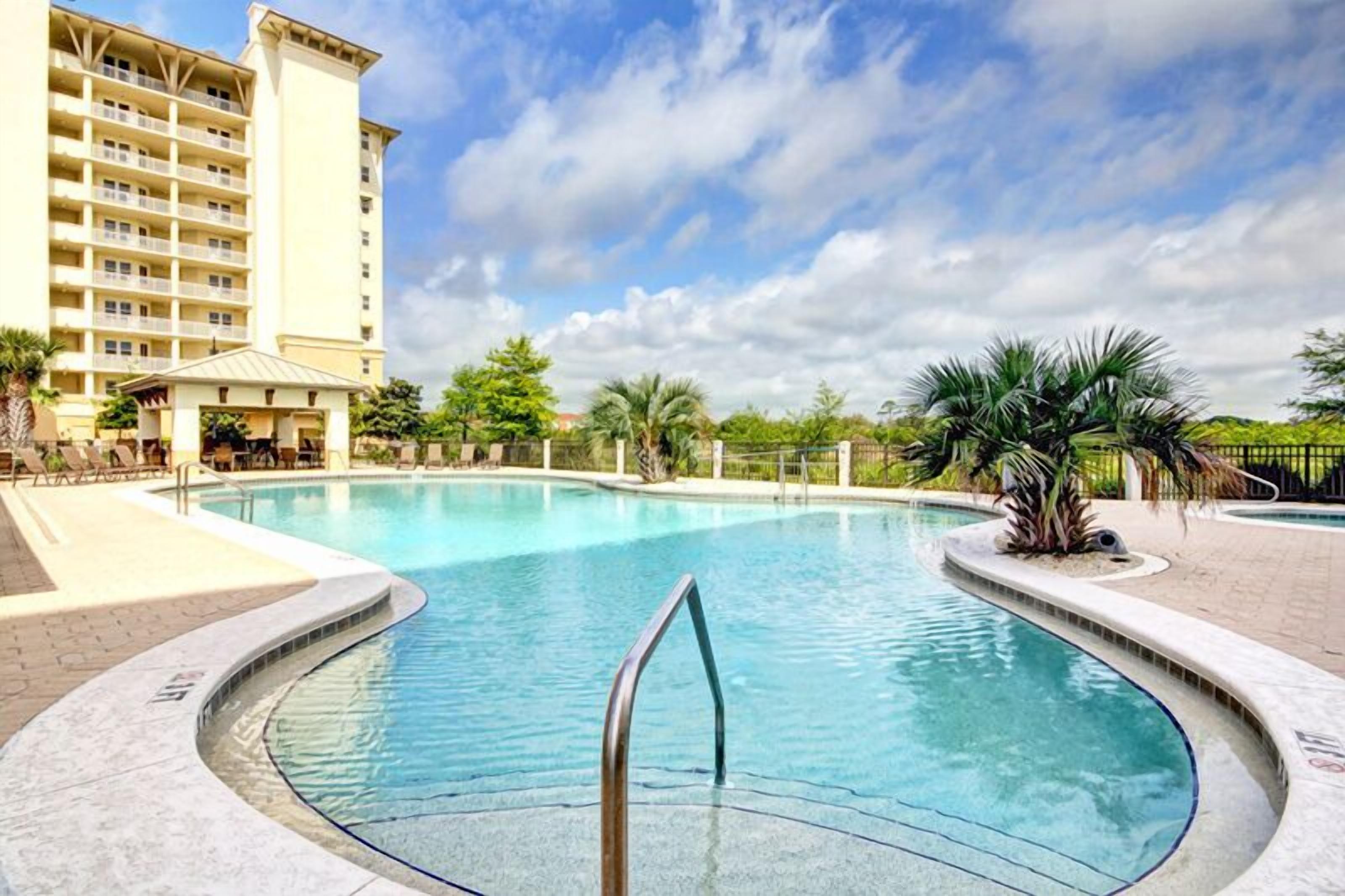 Ein Pool mit gewölbter Kante, eine Palme und ein Hotel im Hintergrund.