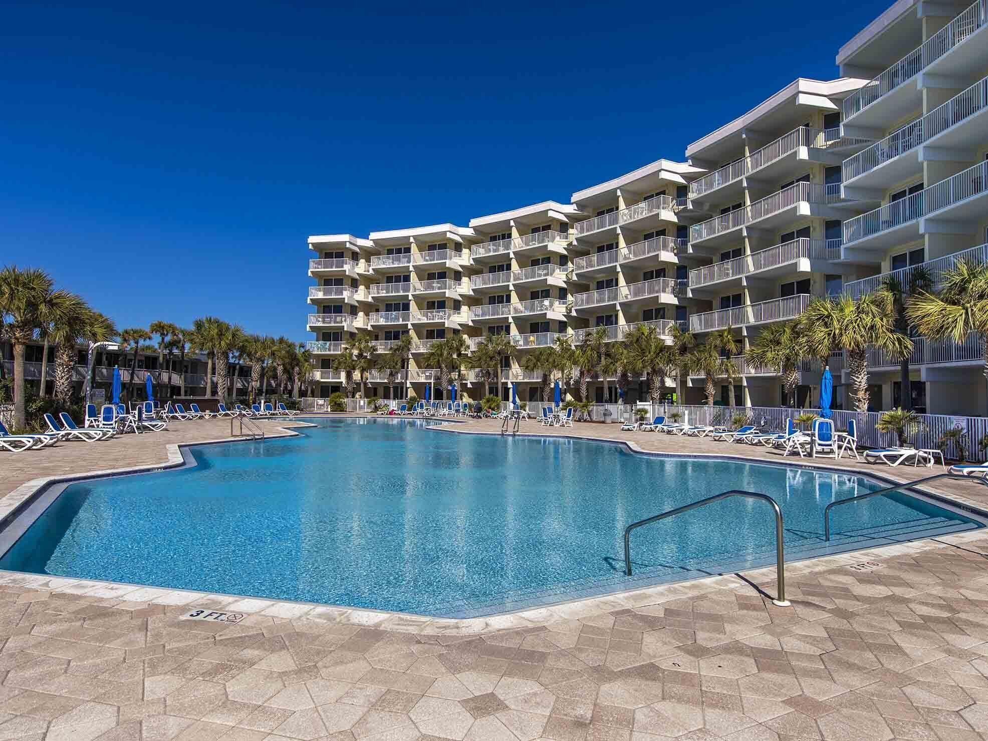 Ein Hotel mit einem großen Pool, umgeben von Liegestühlen und Palmen.