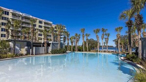 A hotel with a large pool surrounded by palm trees and a clear blue sky.
