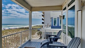 Ein Balkon mit Blick auf Strand und Meer, ausgestattet mit zwei Adirondack-Stühlen und einer kleinen Decke.