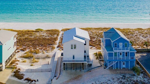 Ein Strandgrundstück mit einem weißen Gebäude und einem blauen Haus, beide mit direktem Blick auf den Ozean.