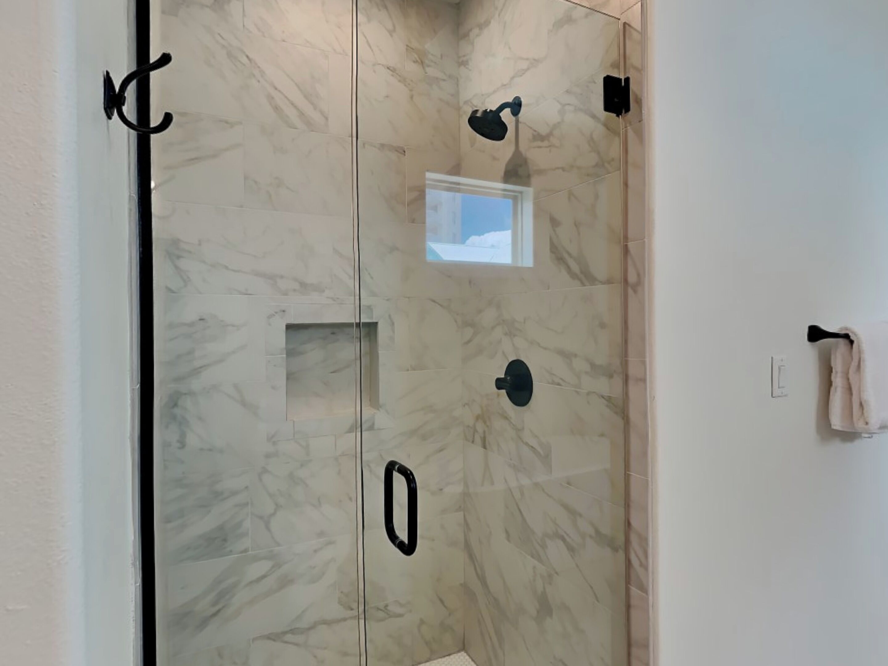 A bathroom with a glass door, a small window, and a towel rack.