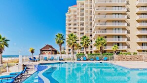 A swimming pool with blue water, surrounded by lounge chairs and palm trees. - Escapes to the Shores #704 by Southern Vacation Rentals (Orange Beach)