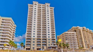 A beachfront hotel with multiple floors, balconies, and a sandy beach in the foreground. - Escapes to the Shores #704 by Southern Vacation Rentals (Orange Beach)
