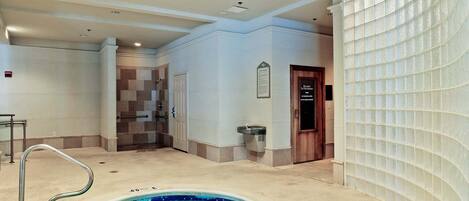 A hotel bathroom with a spa pool, a shower area, and a glass-enclosed door.