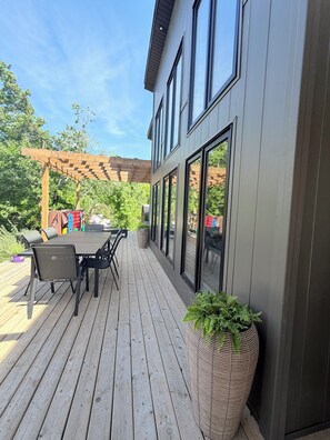 Une terrasse en bois avec une table et des chaises, une pergola et un grand bac à fleurs.