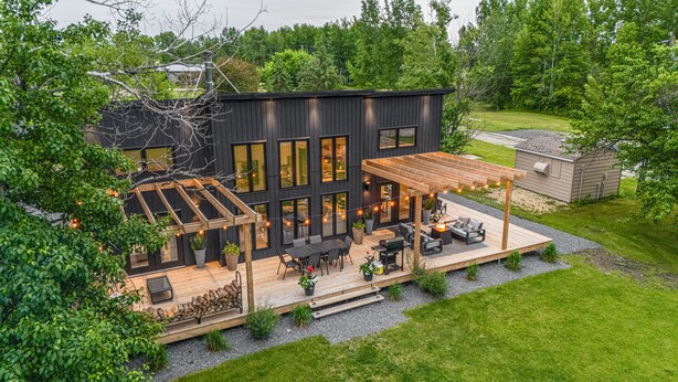 Una casa moderna con terraza, mobiliario exterior y una pérgola.