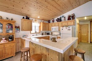 A kitchen with wooden cabinets, a central island with stools, and a wooden ceiling.