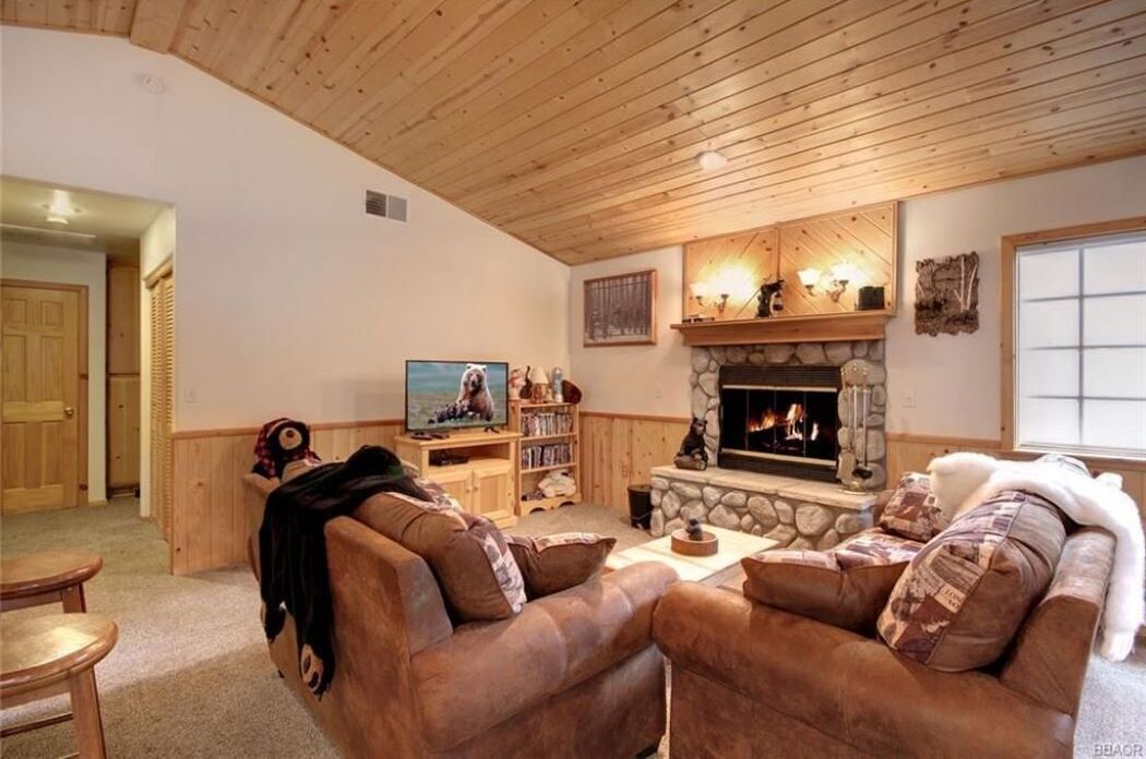 A cozy living room with leather sofas, a stone fireplace, and a television.