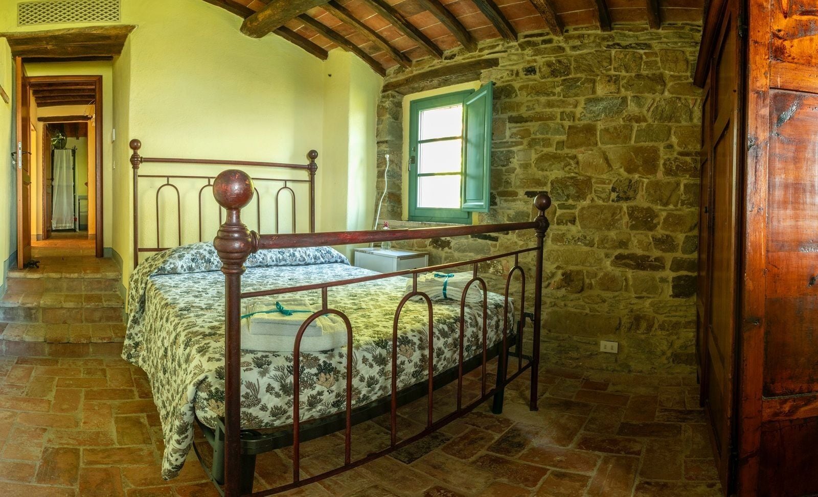A bedroom with a stone wall, a wooden ceiling, and a metal bed frame.