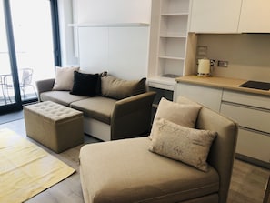 Uma sala de estar moderna com um conjunto de sofás, um banquinho e uma área de cozinha com um laptop no balcão.