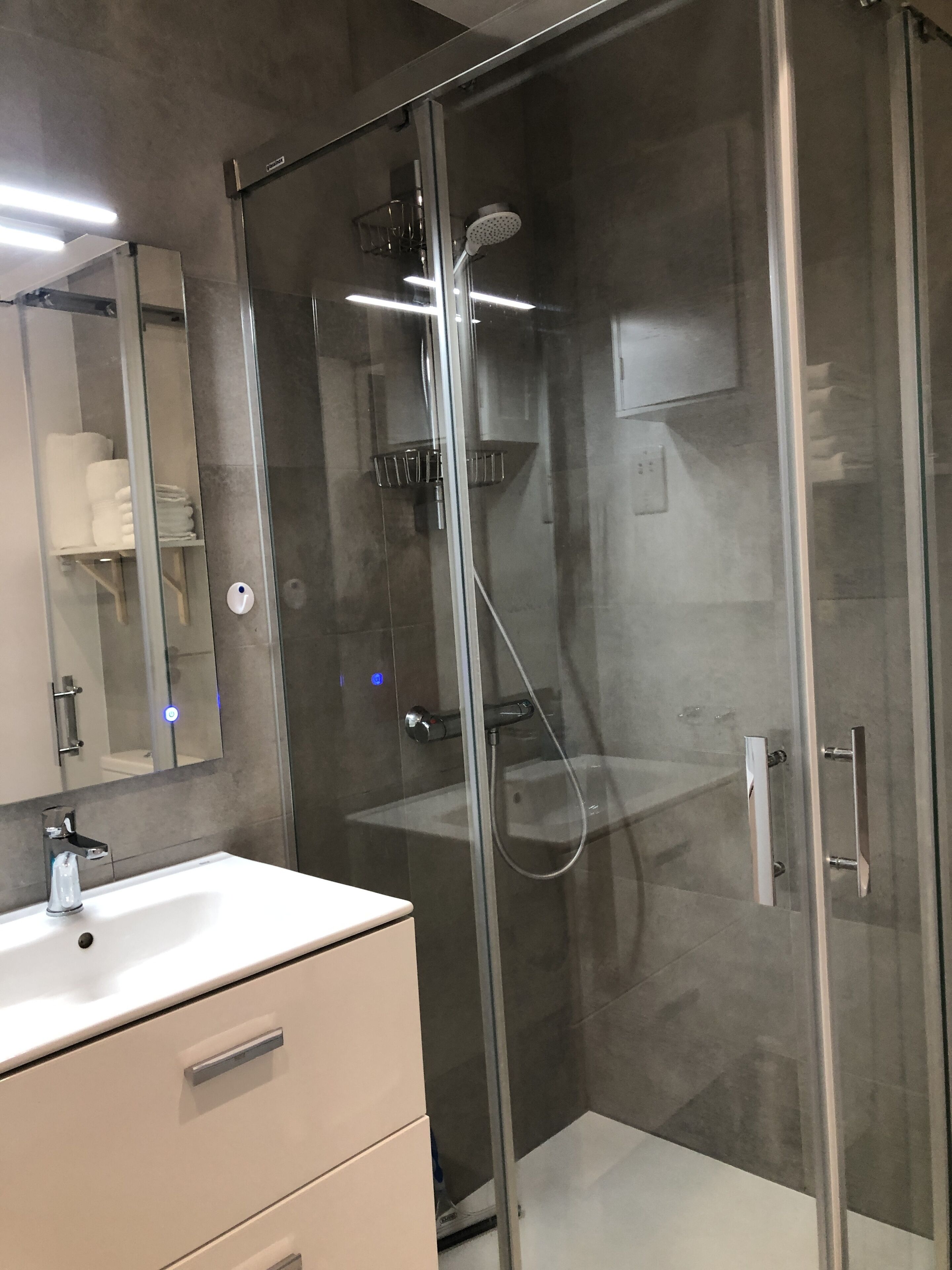 Une salle de bain moderne avec une douche à parois de verre, un lavabo blanc et un miroir.