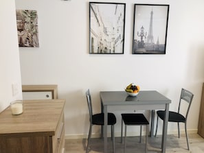 Uma sala de jantar com uma mesa de madeira, uma tigela de frutas e duas cadeiras. Há duas fotos emolduradas na parede.