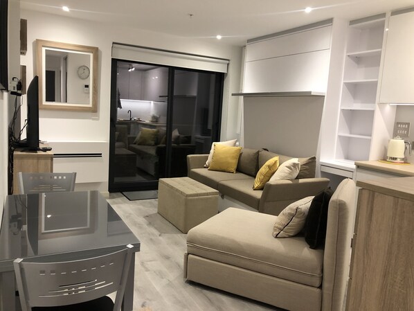 A modern living room with a sofa, ottoman, and a dining area with a glass table.