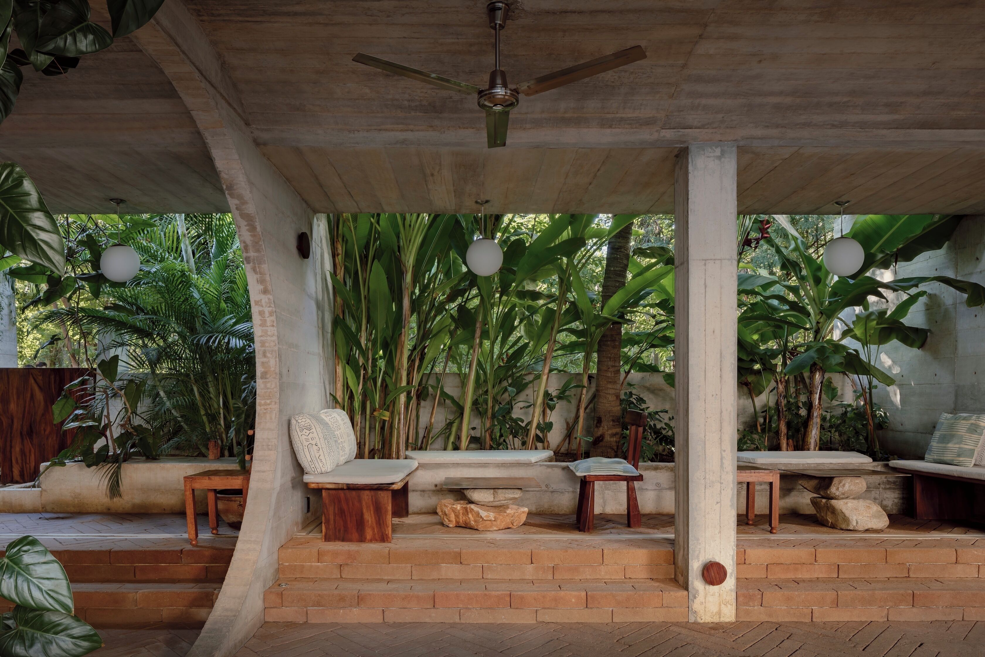 Un espacio de estar al aire libre cubierto, con ventilador de techo, escalones de piedra y diferentes disposiciones de asientos.