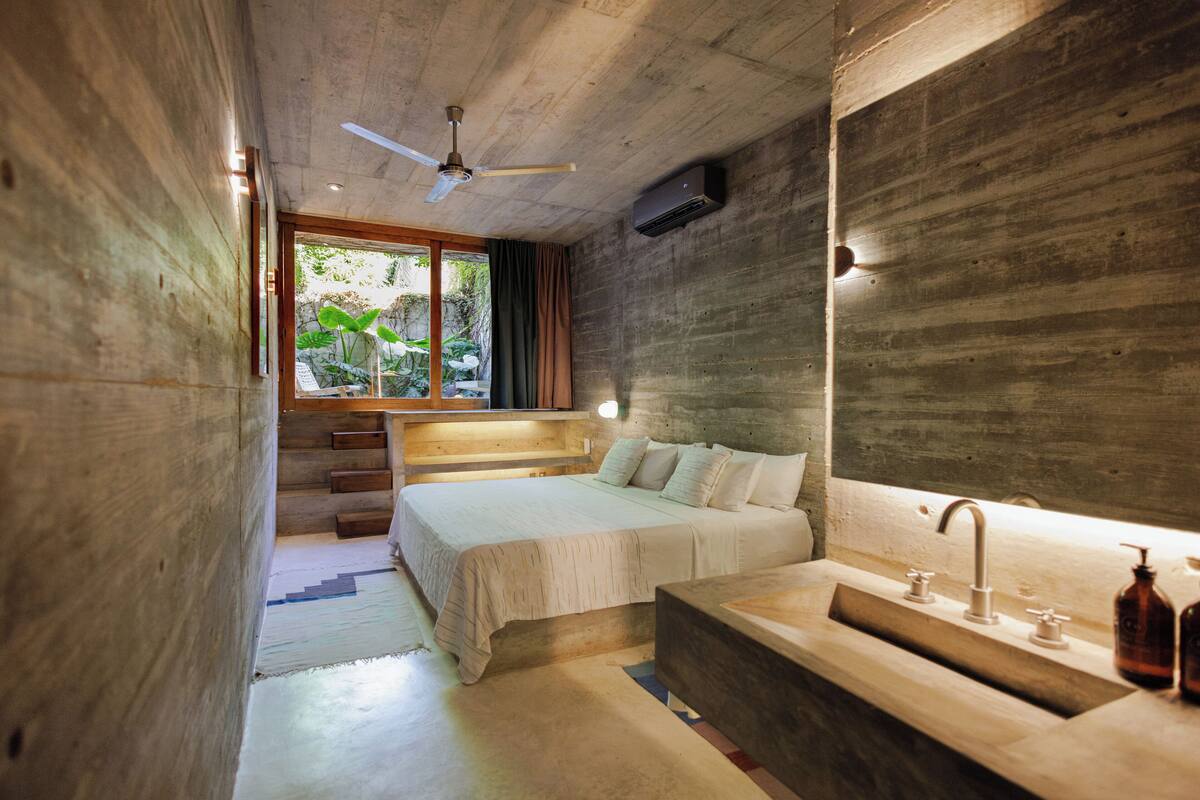 A modern bedroom with a large bed, a built-in bench, a wooden ceiling, and a window with curtains.