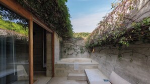 Casa de banho moderna com banheira, cabine de chuveiro em vidro e parede de betão com plantas trepadeiras.