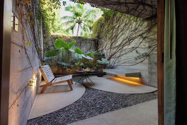 Un espace extérieur paisible, aménagé avec un banc en bois et une table, le tout entouré d’un mur en béton orné de plantes grimpantes.