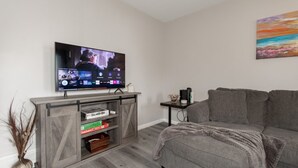 A living room with a flat-screen TV, grey sofa, wooden entertainment unit, and a painting on the wall.