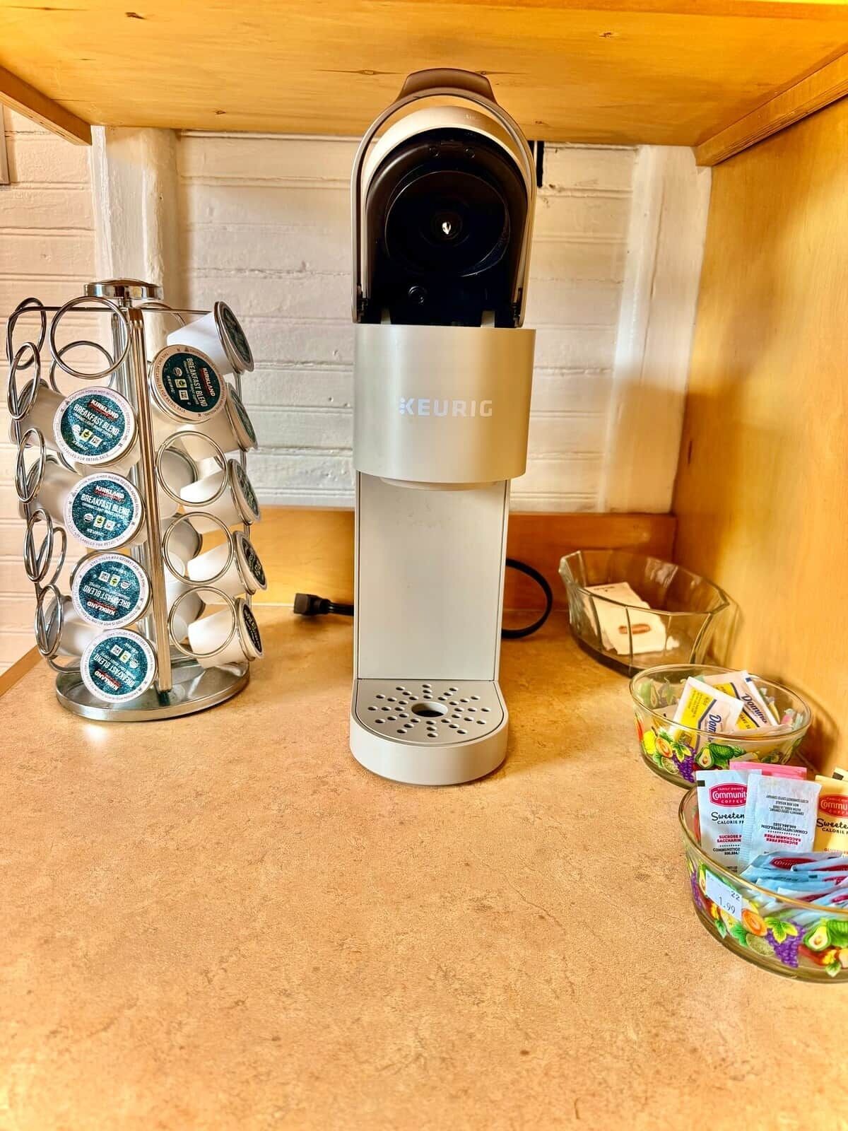 En Keurig-kaffemaskin med ett fack för kaffekapslar, en glasskål med kaffekapslar och ett glas juice.