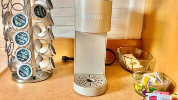 En Keurig-kaffemaskin med ett fack för kaffekapslar, en glasskål med kaffekapslar och ett glas juice.