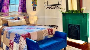 Una camera da letto con un letto, un divano blu, un lampadario, un camino e una finestra con tende.