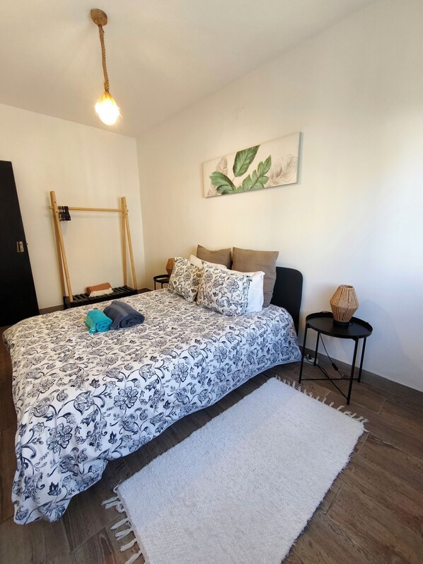 A bedroom with a bed, a bedside table, a lamp, a wall-mounted shelf, and a painting.