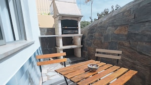 An outdoor patio with a stone wall, a built-in grill, wooden furniture, and a window. - Old Town & 10 min from Beach, Lagos (Lagos)