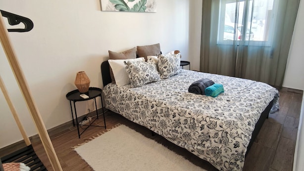 A bedroom with a bed, a bedside table, a hanging light fixture, a window with curtains, and a wall-mounted plant. - Old Town & 10 min from Beach, Lagos (Lagos)
