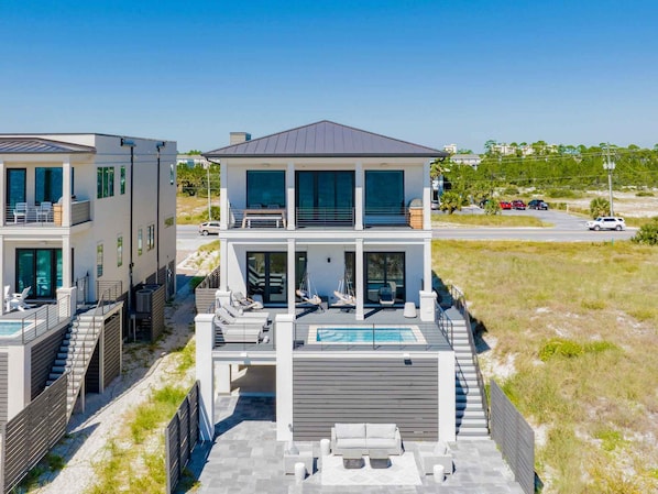 A modern two-story house with a pool, outdoor seating, and a view of the beach.