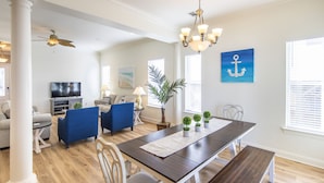 A spacious living room with a dark wooden dining table, blue upholstered chairs, and a large potted plant. - Sandy Retreat by Southern Vacation Rentals (Destin)