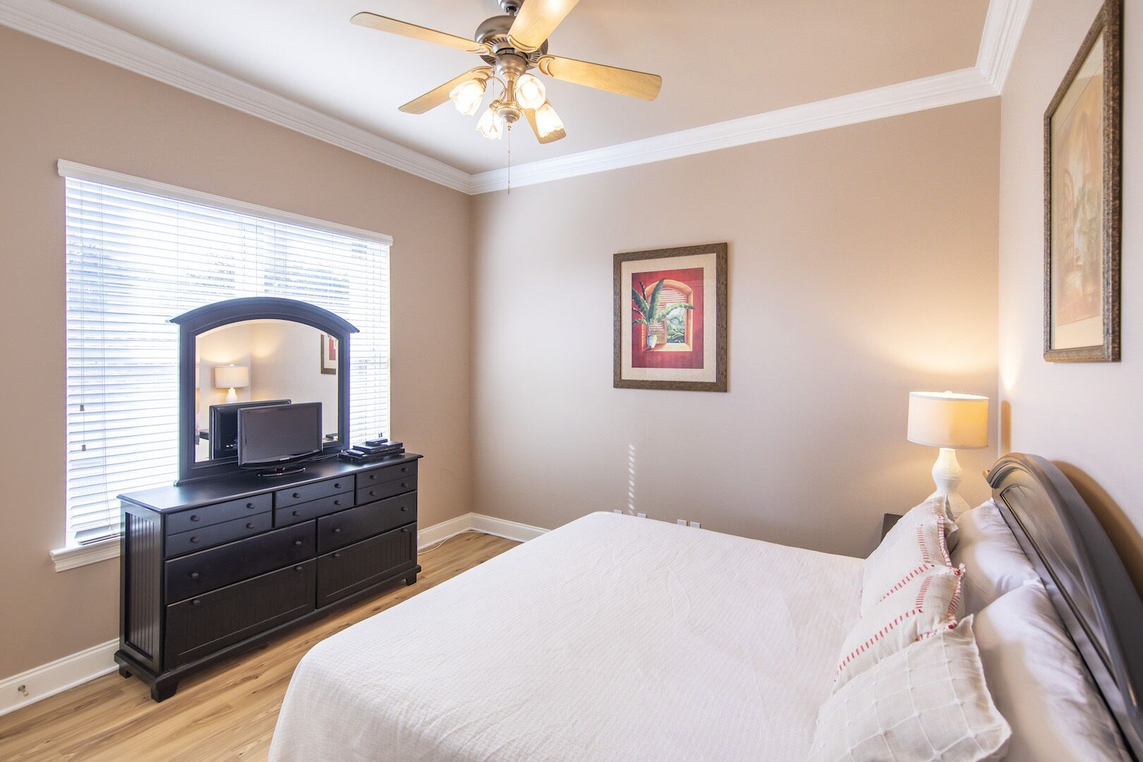 A bedroom with a bed, dresser, ceiling fan, and a window with blinds.