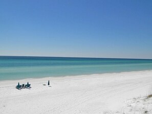A beach with white sand and a clear blue sea. There are a few umbrellas and lounge chairs in the distance. - Layze Dayze by Southern Vacation Rentals (Santa Rosa Beach)