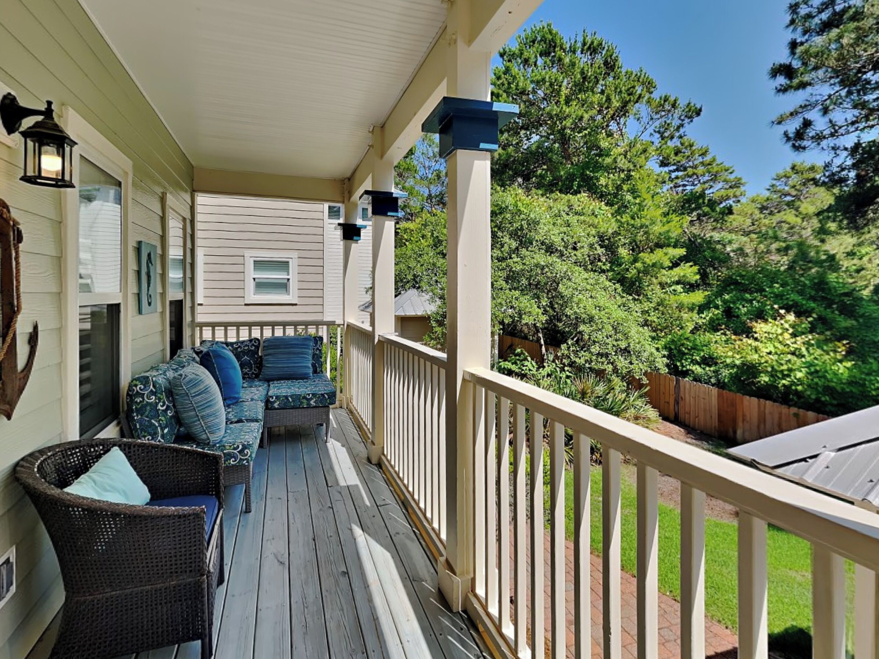 A covered porch with a seating area, a wooden deck, and a view of a backyard with trees and a fence.