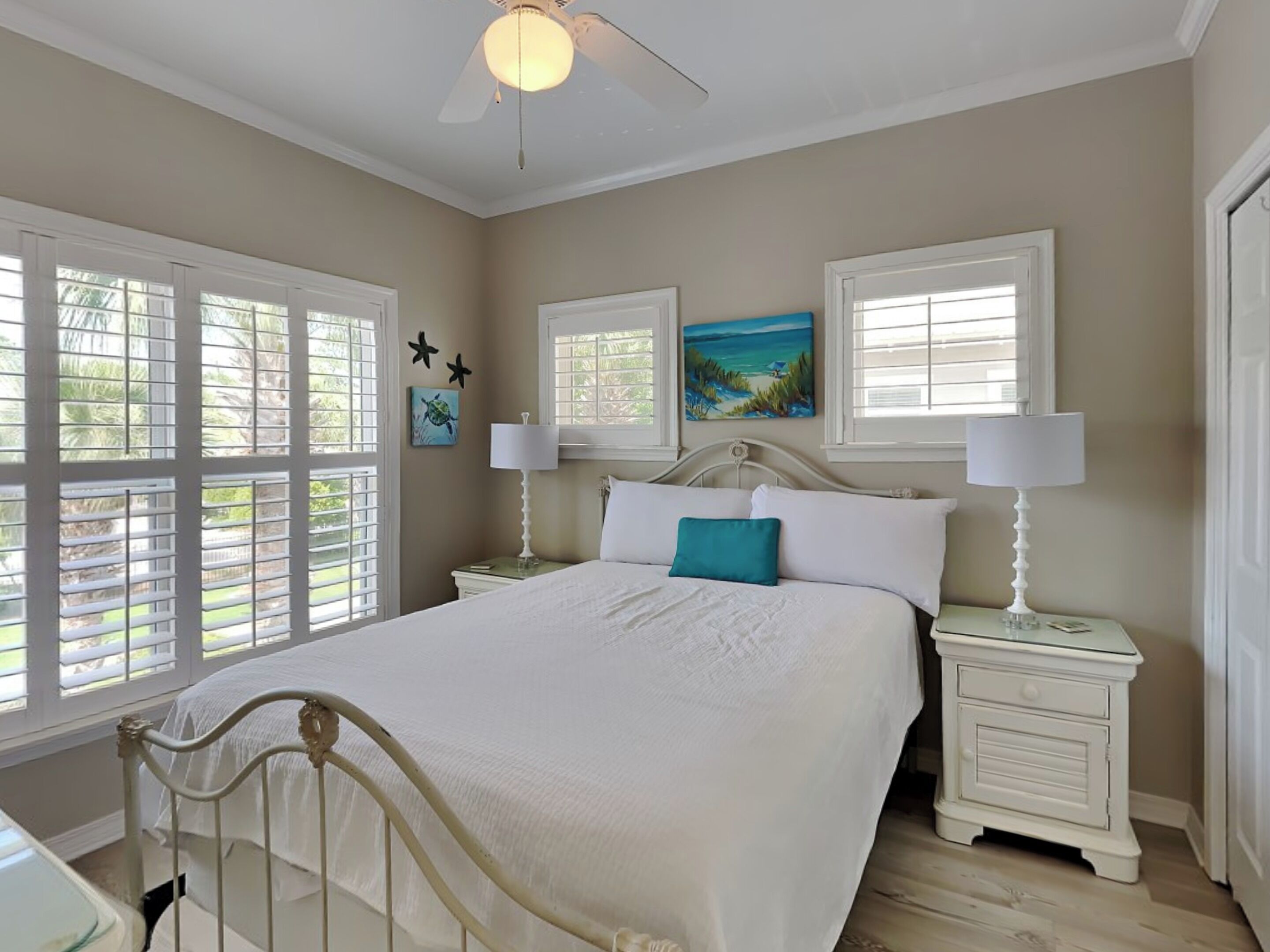 A bedroom with a bed, two bedside tables, a ceiling fan, and windows with blinds.