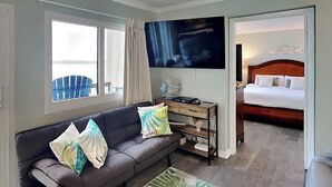 Une chambre d’hôtel avec un canapé gris, une télévision, une table de chevet en bois et un lit avec une tête de lit en bois.