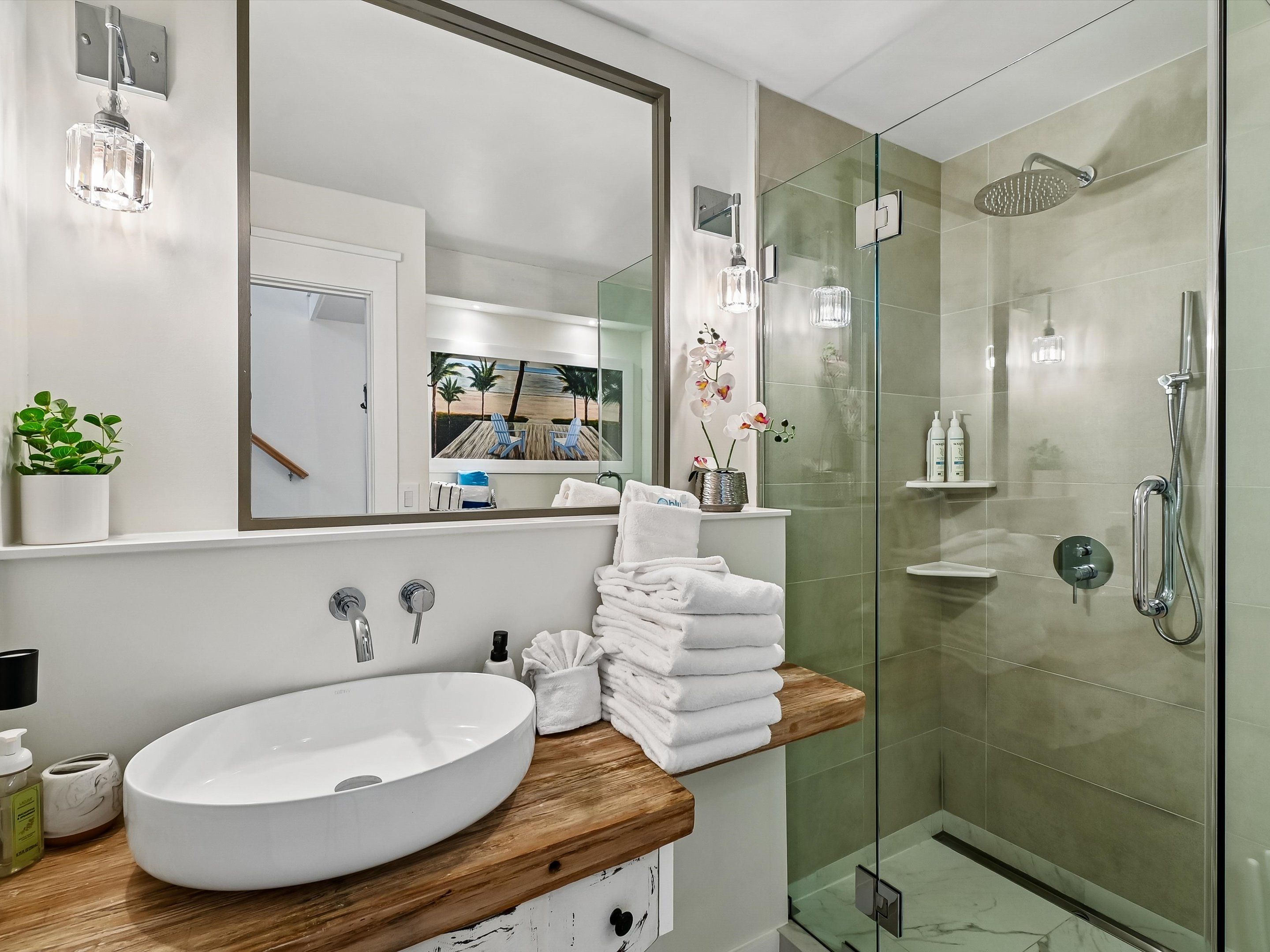A modern bathroom with a large mirror, a round sink, a glass-enclosed shower, and a wooden countertop.