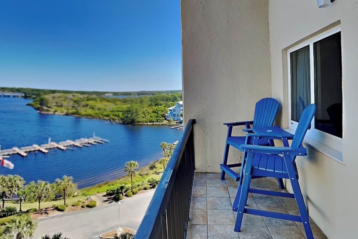 A balcony with two blue chairs, a view of a lake, and a dock.