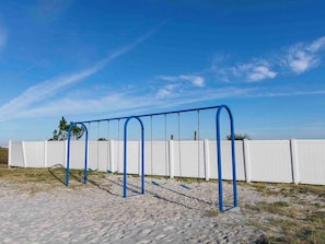 Children can play on the playground with a swing set in a secure, fenced area.