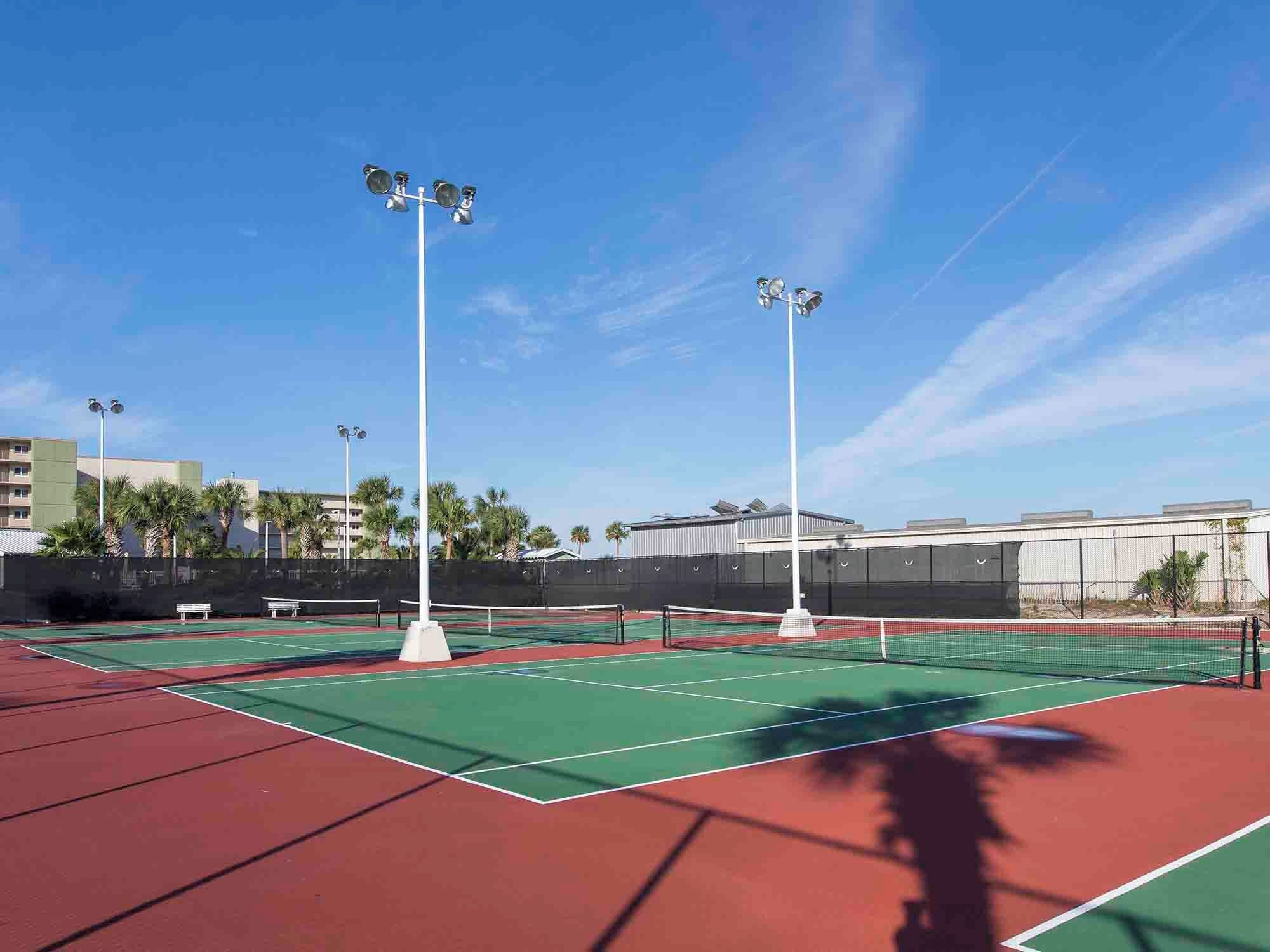An outdoor tennis court with four floodlights, a net, and a green playing surface.